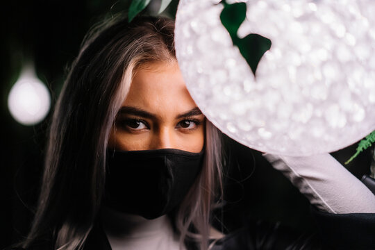 Young woman wearing protective face mask in front of light lamp
