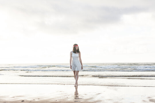 Young woman wearing white dress walking at shore against sea
