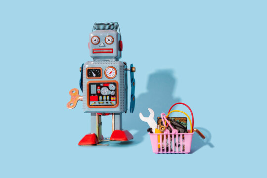 Studio shot of vintage robot toy standing by miniature shopping basket filled with electronic equipment