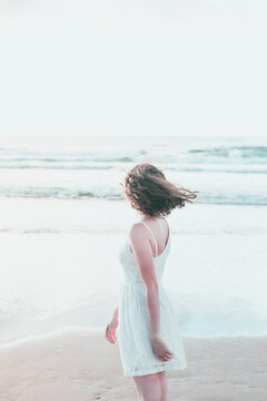 Young woman wearing white dress looking at sea against clear sky