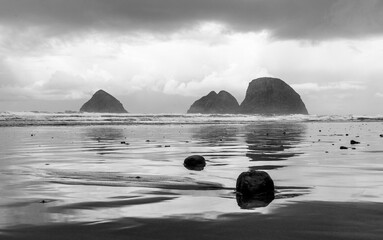 Three Arch Rocks with reflection and smaller stones in sand.