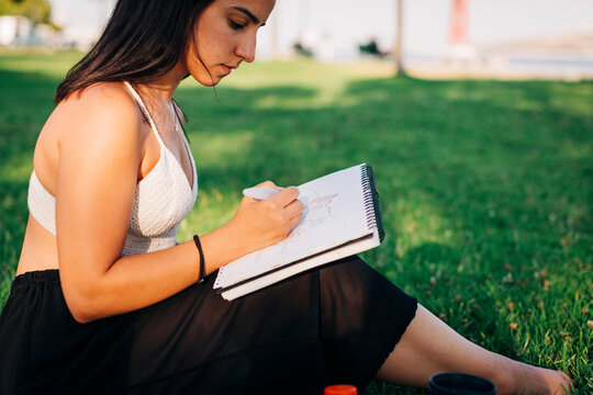 Beautiful woman painting on book while sitting in public park
