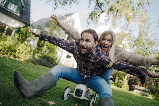 Laughing couple, pretending to fly on a toy car in the garden