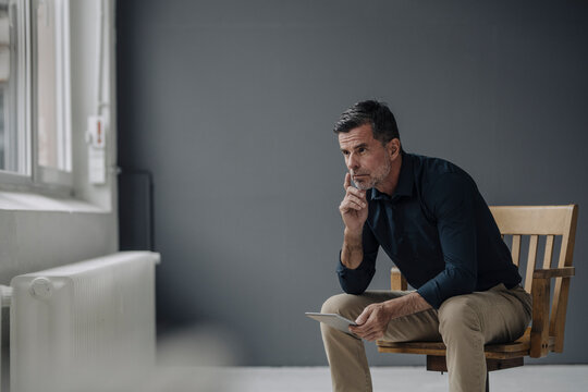 Mature businessman sitting on chair with tablet