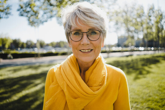 Portrait of smiling mature woman with grey hair wearing glasses and yellow clothes