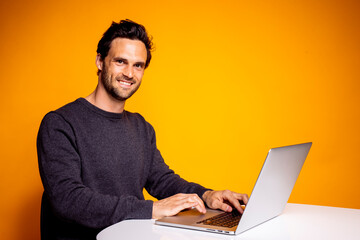 Handsome mid adult man sitting with laptop at table against yellow background