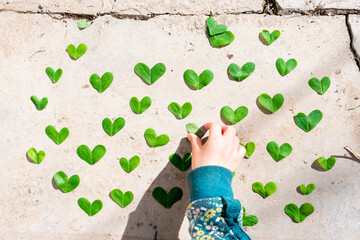 Girl arranging heart shaped green leaves pattern on cement