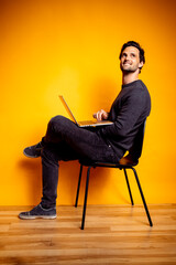 Handsome man looking away while sitting with laptop on chair