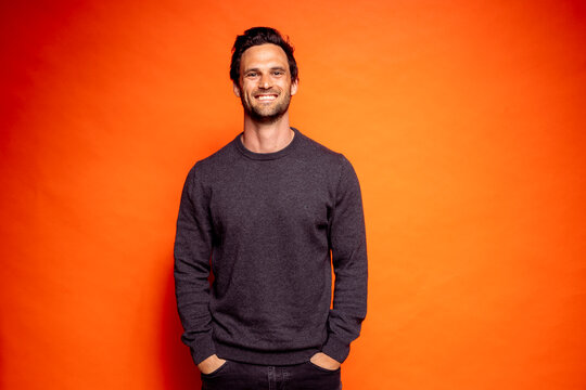 Happy handsome man with hands in pockets against orange background