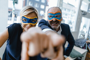 Businessman and woman, wearing super hero masks, pointing at camera
