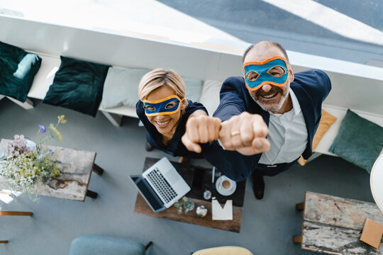 Businessman and woman wearing super hero masks, raising fists