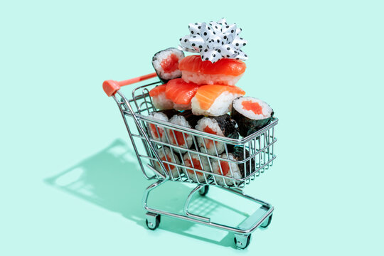 White ribbon on top of fresh salmon sushi nigiri stacked in small shopping cart against mint green background