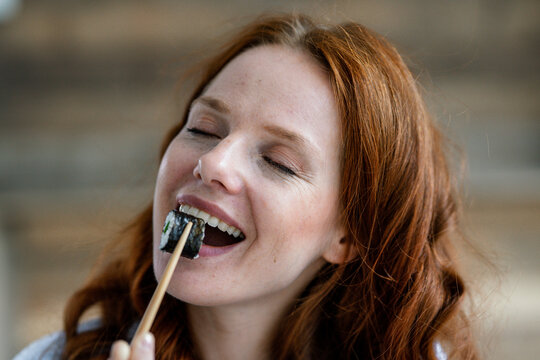 Portrait of happy redheaded woman eating sushi