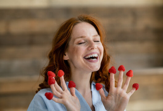 Portrait of laughing redheaded woman with raspberries on her fingertips