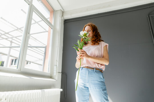 Redheaded woman smelling white peony