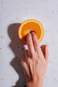 Woman's fingers in halved orange on modern terrazzo marble