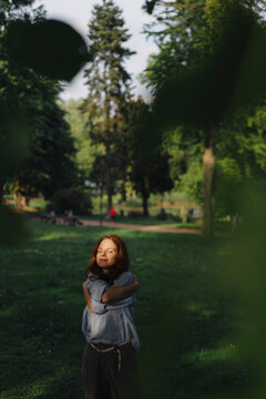 Redheaded woman in a park hugging herself