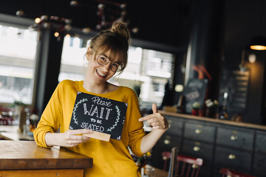 Young woman in a restaurant holding 'wait to be seated' sign