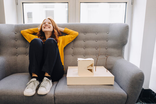 Happy woman sitting on couch next to architectural model