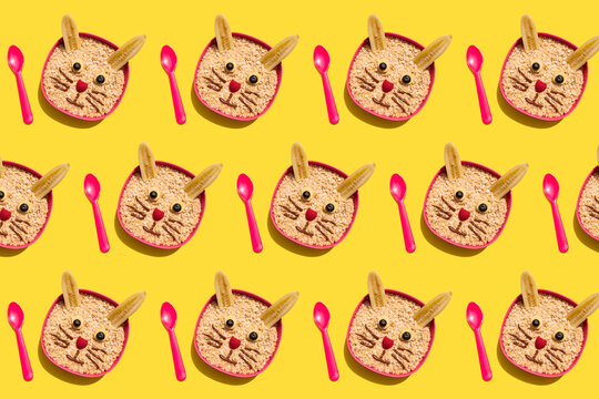 Pattern of bowls of avena porridge with rabbit faces made of bananas, chocolate, raspberries and blueberries