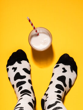 Man's foot with cow print socks and glass of milk on yellow background