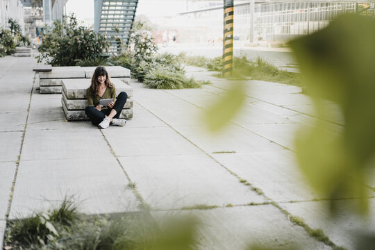Young smiling woman sitting on the ground and using tablet
