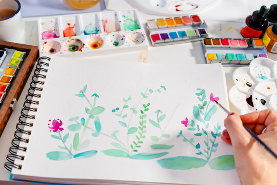 Woman painting botanical plants and flowers on paper at table
