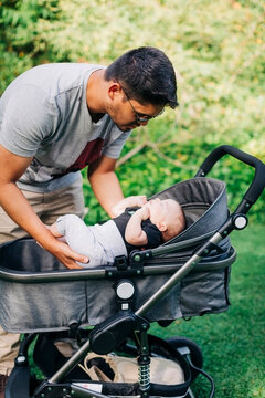 Young man putting baby boy in carriage at park