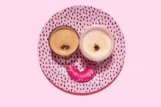 Anthropomorphic face made of plate, halved doughnut and two glasses of coffee
