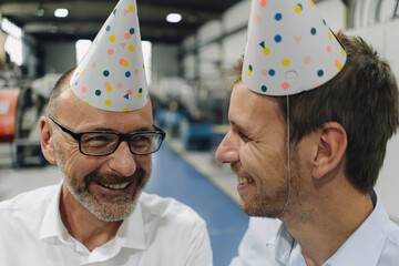 Portrait of two happy businessmen wearing party hats in a factory
