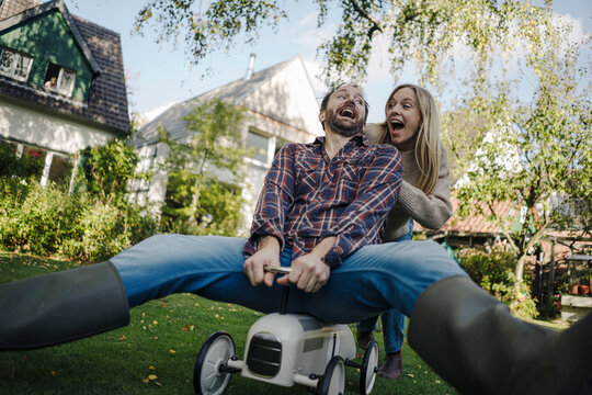 Laughing couple pretending to ride a toy car in the garden
