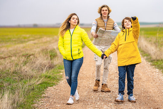 Three siblings hiking with map along dirt road