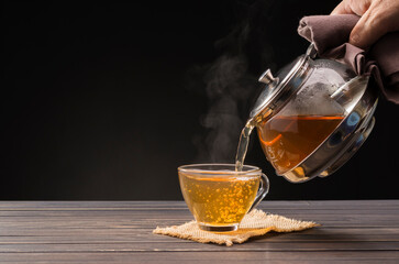 Tea ceremony process Tea ceremony A freshly brewed cup of black tea is placed on a wooden table where a warm soft light shines against a dark black background.