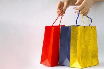 Women's hands hold red, blue and gold paper bags with purchases on a white background. Copyspace