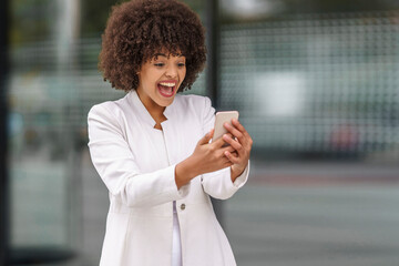 Happy businesswoman looking at mobile phone while standing outdoors
