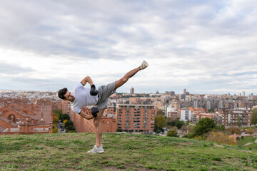 Male acrobat practicing kickboxing against cloudy sky over city