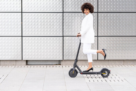 Businesswoman riding electric push scooter against silver wall