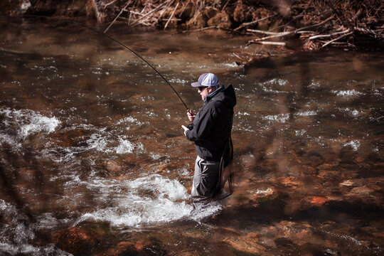 Fly fisherman casting in rapid flowing river at forest