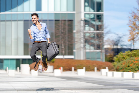 Excited businessman holding briefcase while jumping on footpath