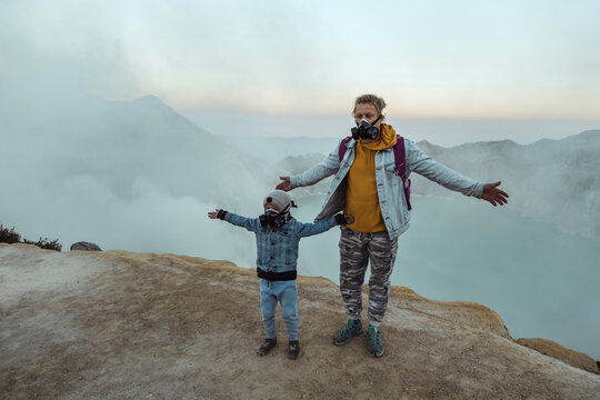 Father and son with respirator masks standing at the edge of volcano Ijen, Java, Indonesia