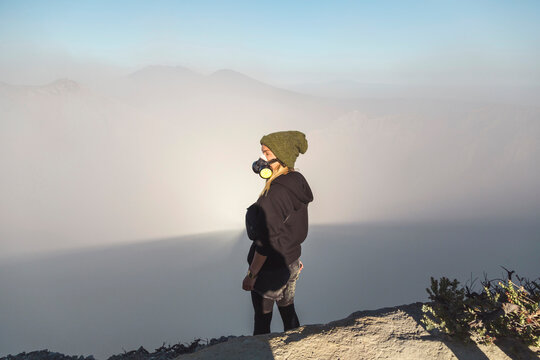 Young woman with respirator mask standing at the edge of volcano Ijen, Java, Indonesia
