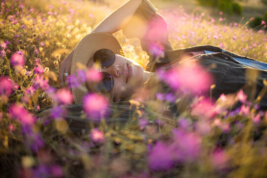 Young woman with sunhat lying on meadow at sunset