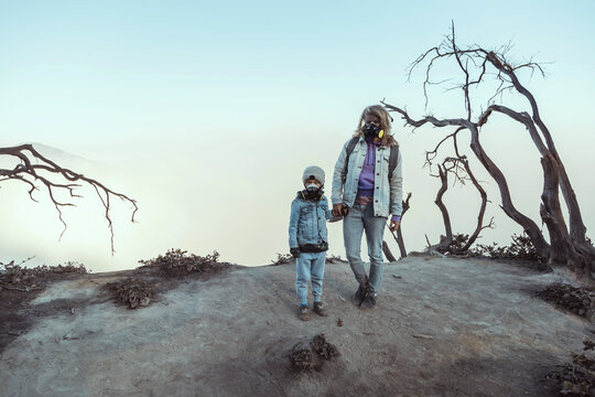 Mother and son with respirator masks standing hand in hand at the edge of volcano Ijen, Java, Indonesia