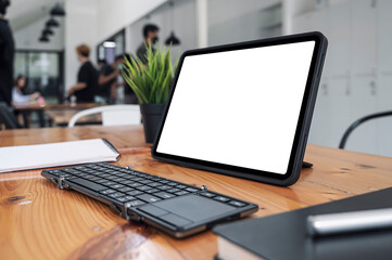 Mockup blank white screen portable tablet and keyboard in co-workspace.