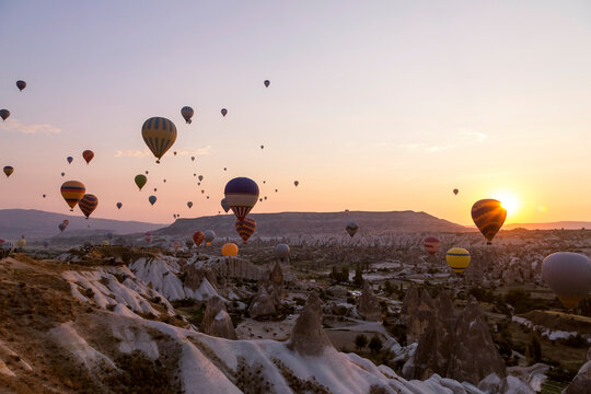Fototapeta Colorful hot air balloons flying over rocky landscape at sunset in Goreme, Cappadocia, Turkey