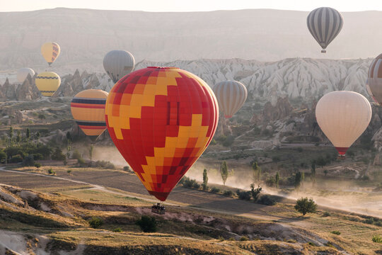 Multi colored hot air balloons flying over land at Goreme National Park during sunset, Cappadocia, Turkey