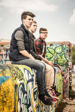 Group of friends sitting on a graffiti wall in an old run down industrial area