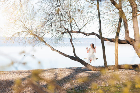 Full length of woman enjoying swing from bare tree against lake