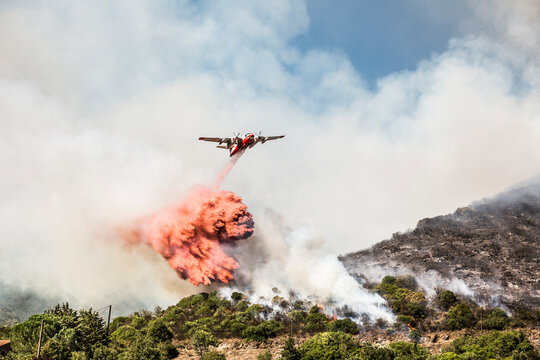 Aerial fire fighting aircraft dropping load of flame retardant on wildfire, Corsica, France
