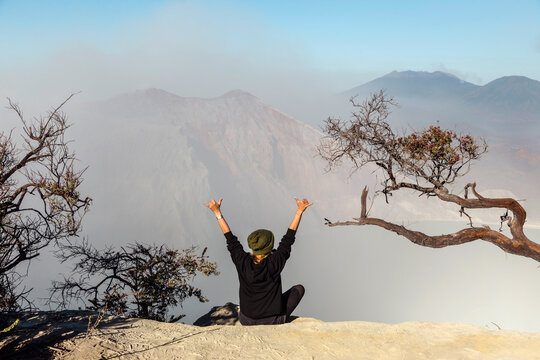 Woman with respirator mask sitting at volcano Ijen and  raising her arms, Java, Indonesia